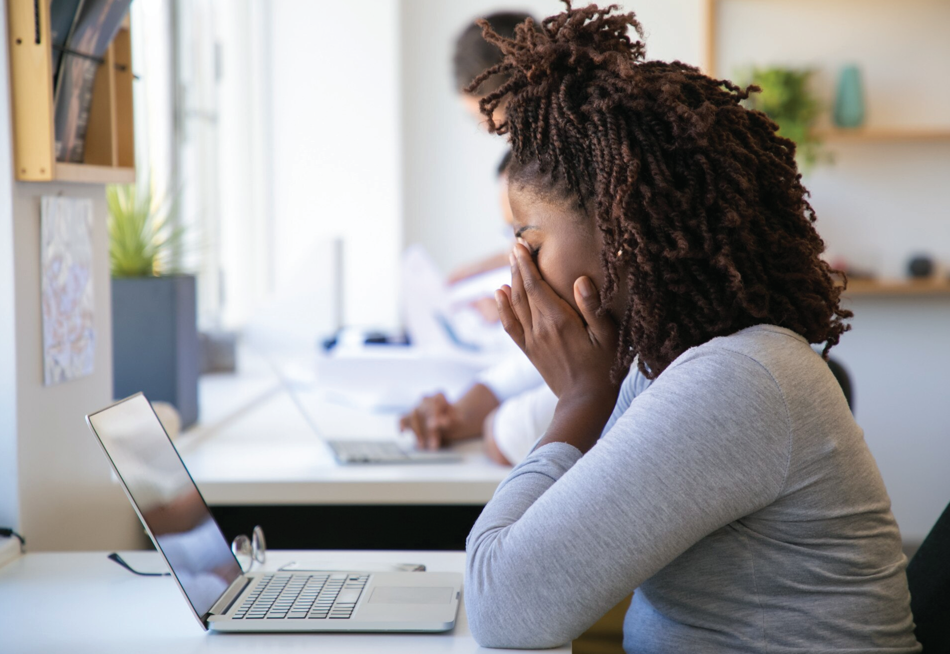 Image of young woman feeling stressed, looking down and covering her face. Image signifies how a care partner may feel when handling work and caring for a loved one.